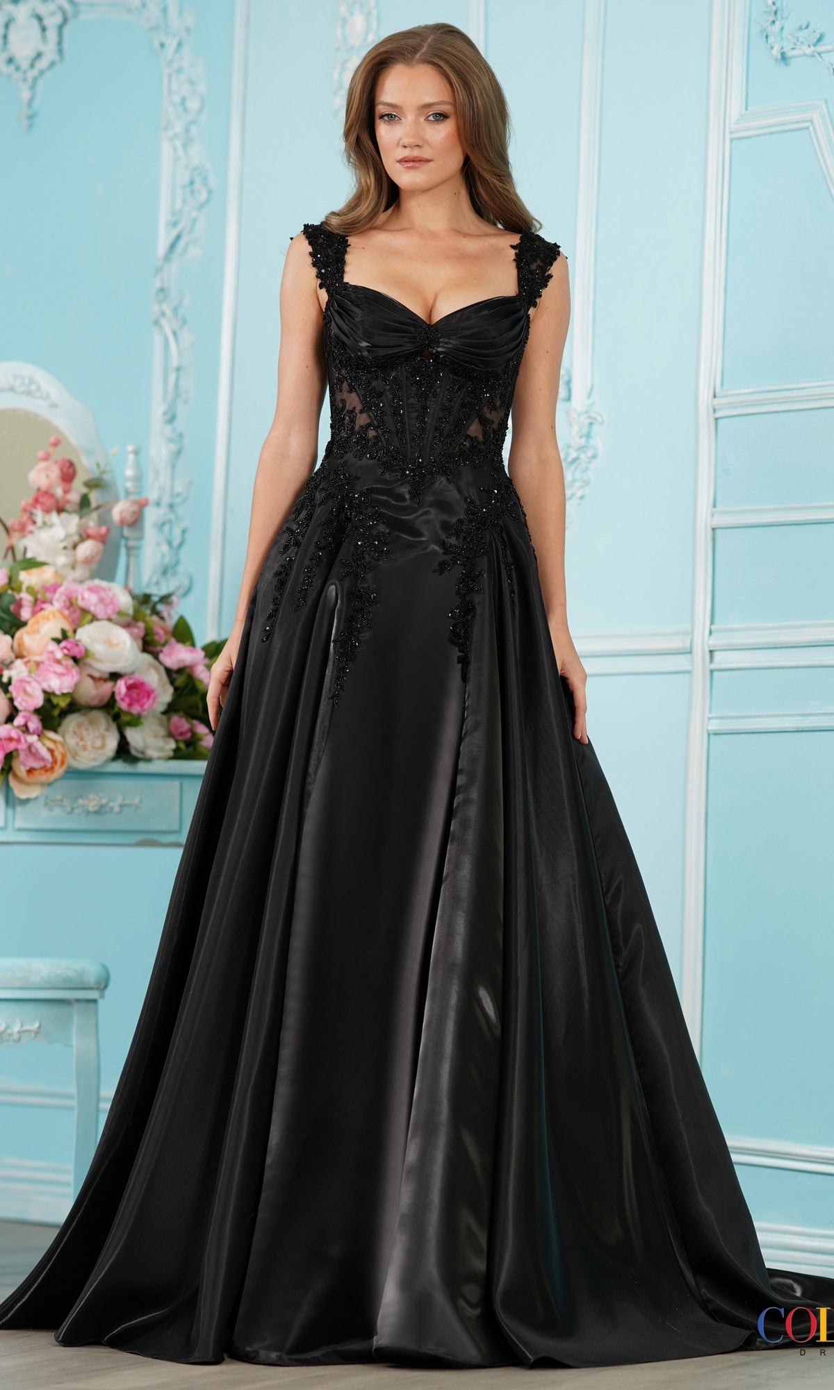 A woman wears a black Long Prom Dress: Colors Dress 4150, an off-the-shoulder lace gown featuring a sweetheart neckline, corset-style bodice, and beaded embroidery at the waist.